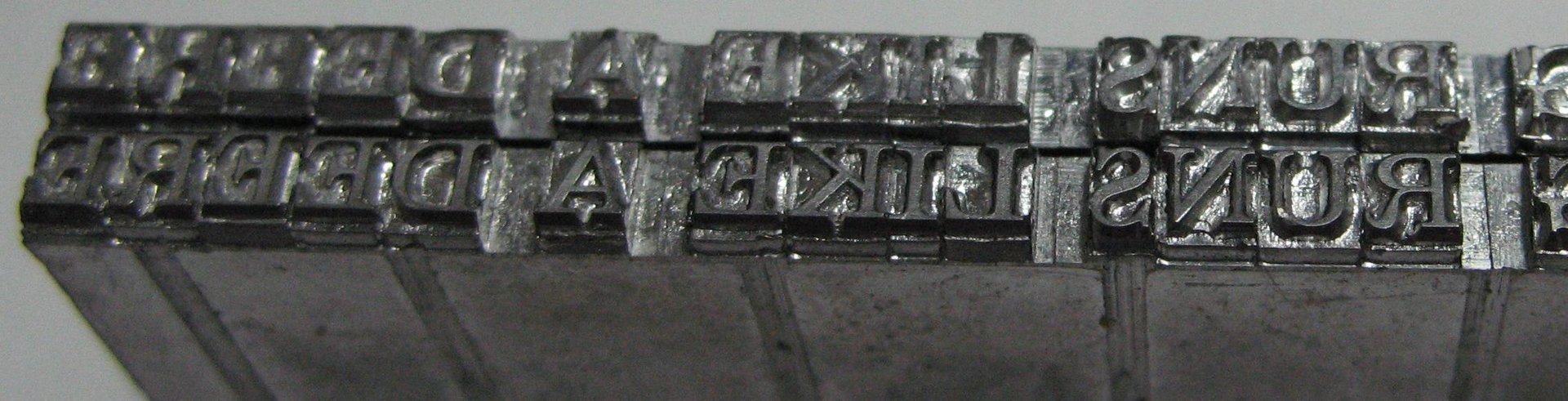 Linotype slugs — cast metal lines of type, each break determined before the ink touched paper. Photograph by Dale Mahalko, 2008 (cropped), CC BY-SA 3.0.
